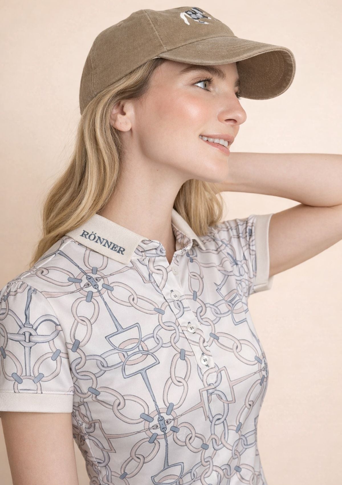 Woman wearing a patterned polo shirt and cap with 'RÖNNER' branding on a beige background