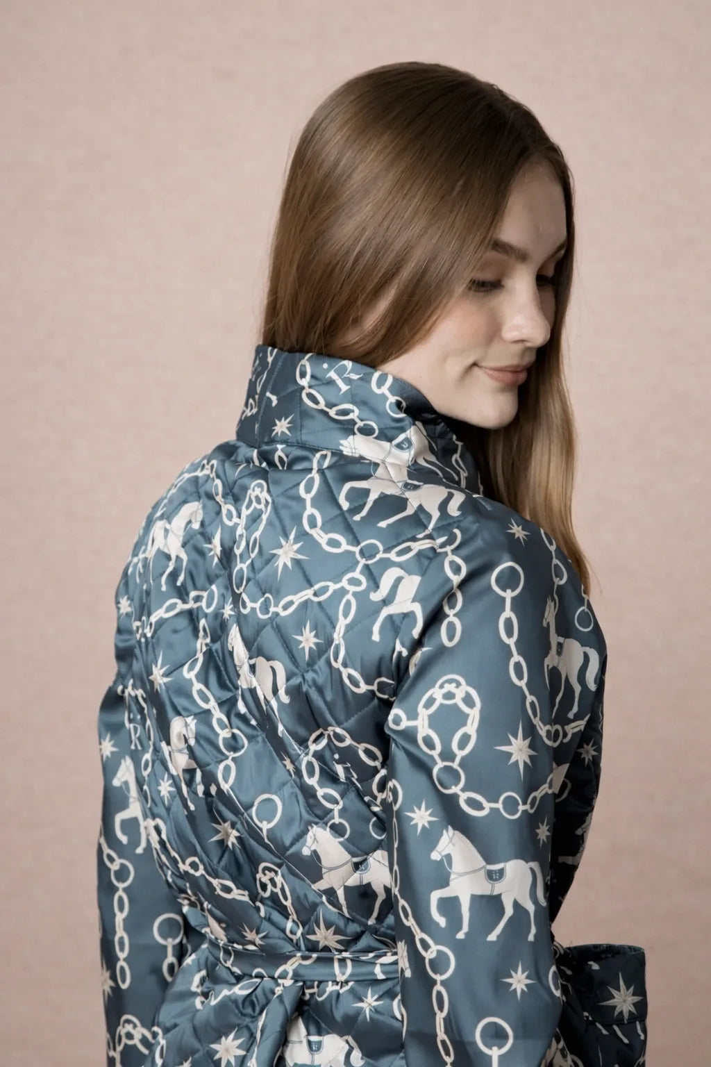 Woman wearing a blue patterned coat with horses and stars on a beige background