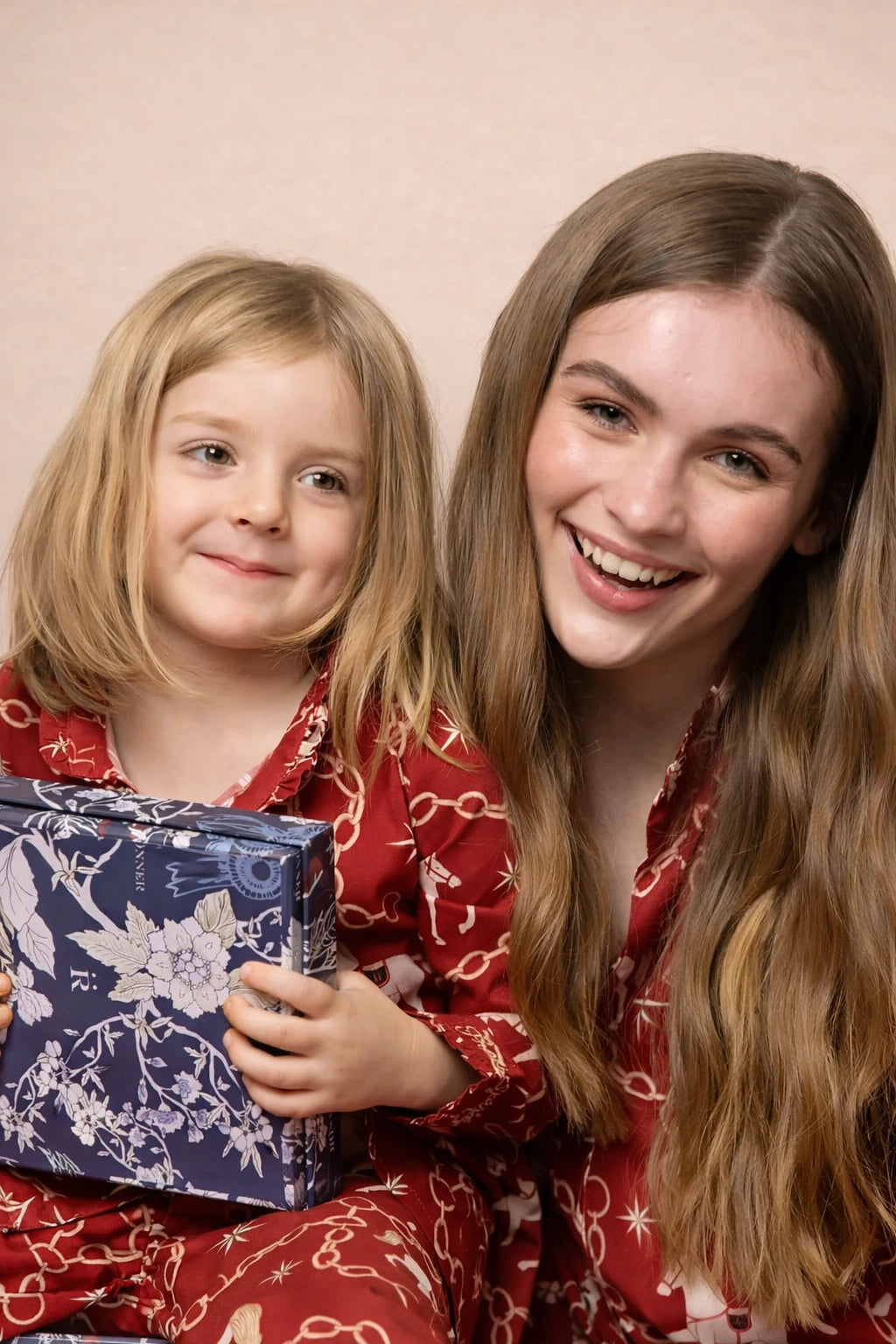 Two people in red pajamas holding a wrapped gift against a pink background