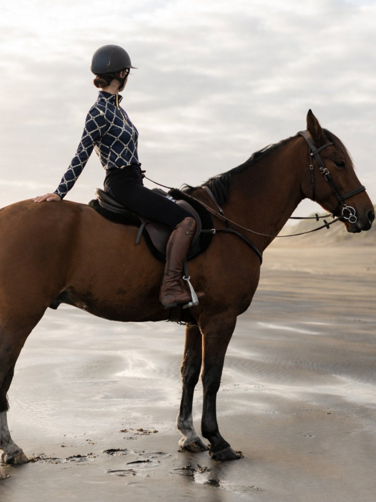 Person riding a horse on a beach with a cloudy sky.